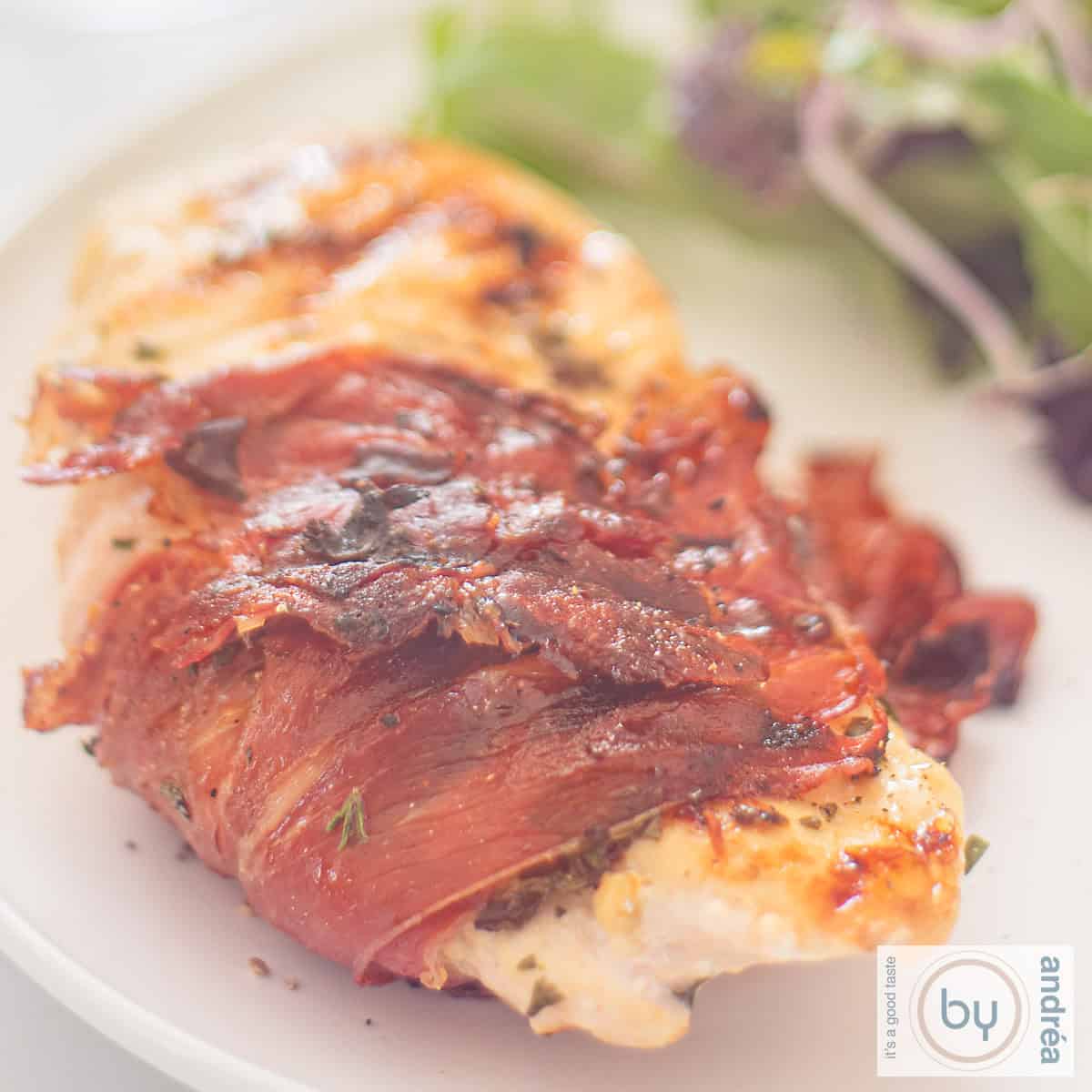 Een vierkante foto met een kipfilet met Italiaanse kruiden in serranoham gewikkeld