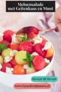 Een deel van een kom met drie meloensoorten, geitenkaas, honing en munt. Een tekst bovenin: meloensalade met geitenkaas en munt