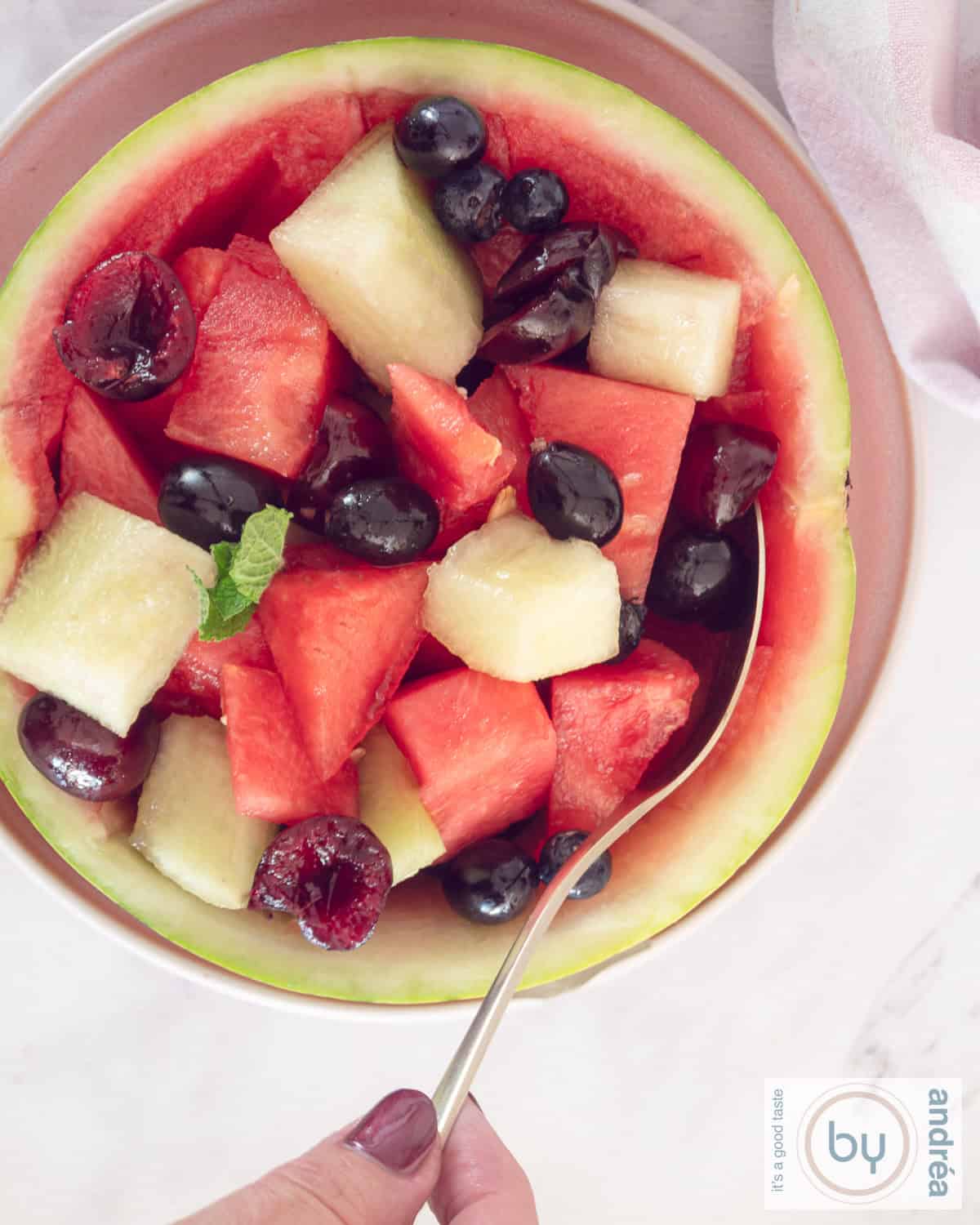 A photo from above of a melon, hollowed out and filled with grapes, melon and cherries