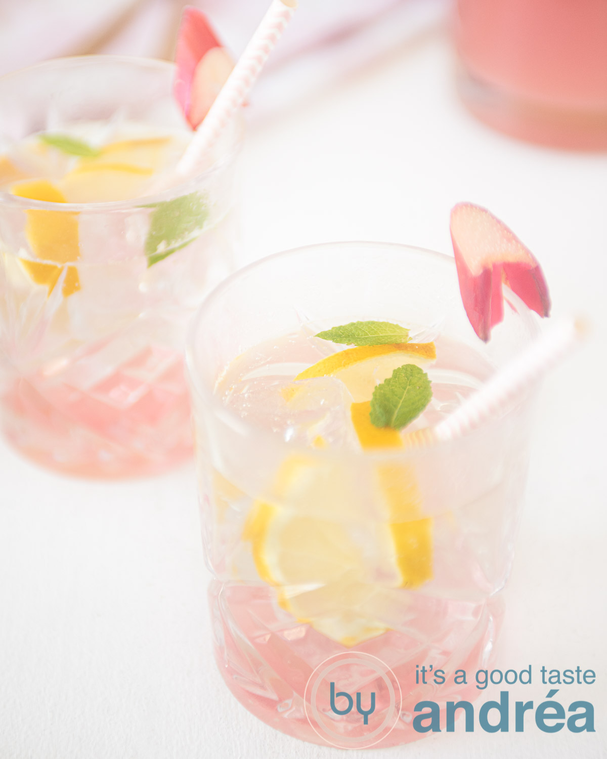 Twee glazen met Rabarber ijsthee schuin achter elkaar op een witte ondergrond