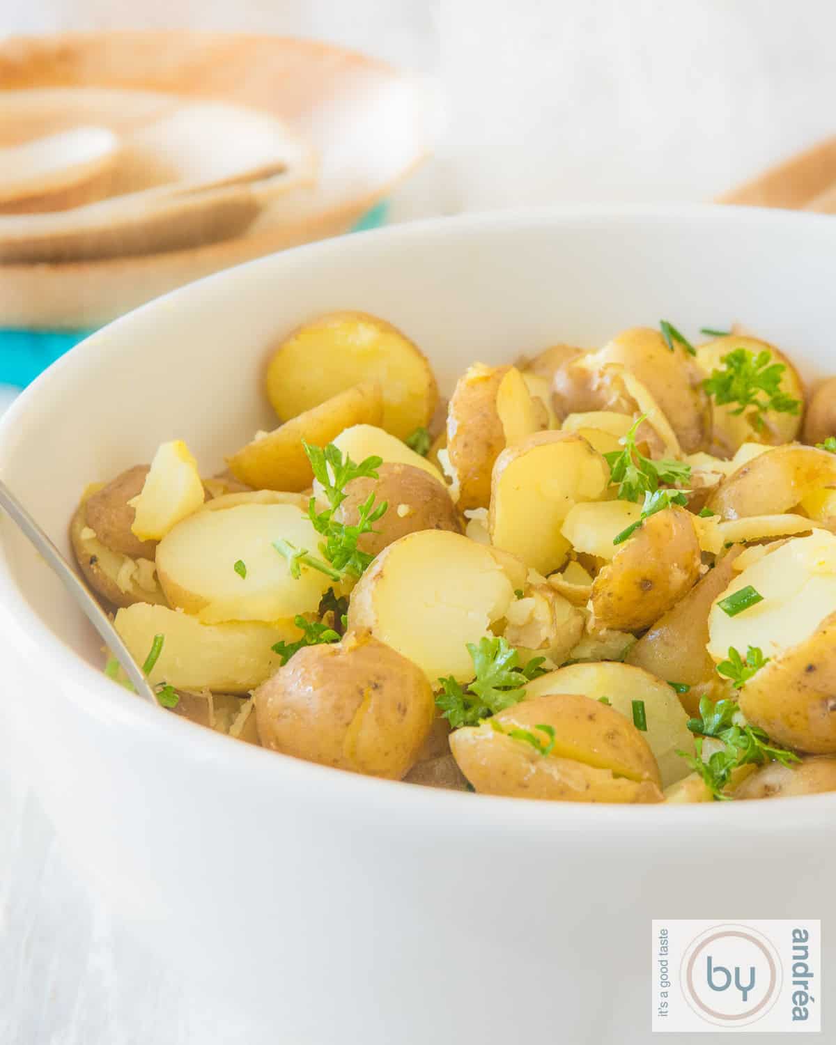 Een deel van een witte schaal gevuld met gehalveerde krieltjes en kruiden. 