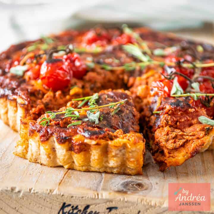 Een vierkante foto met bolognese quiche met een part eruit gesneden.