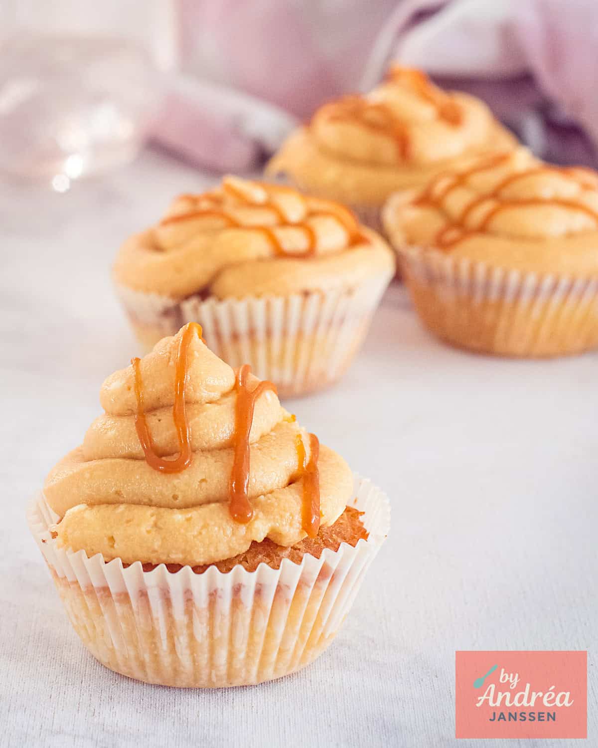 Een cupcake in de voorgrond met vanille smaak en een gezouten karamel topping en frosting. In de achtergrond nog drie cupcakes