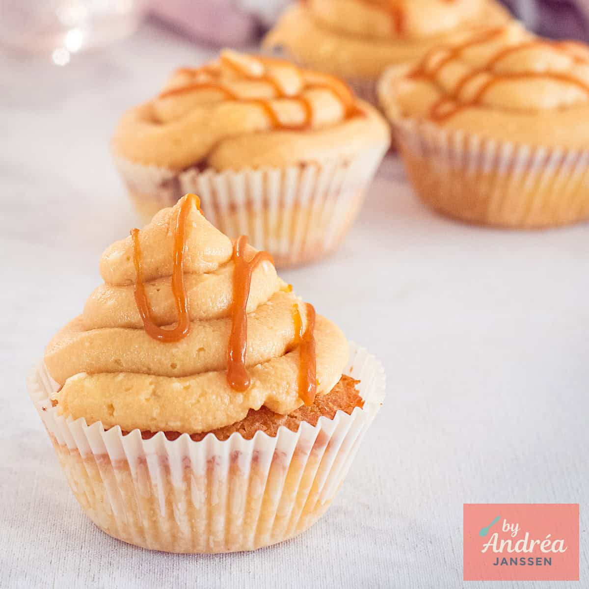 Een vierkante foto met vier cupcakes met frosting en een salted caramel topping.