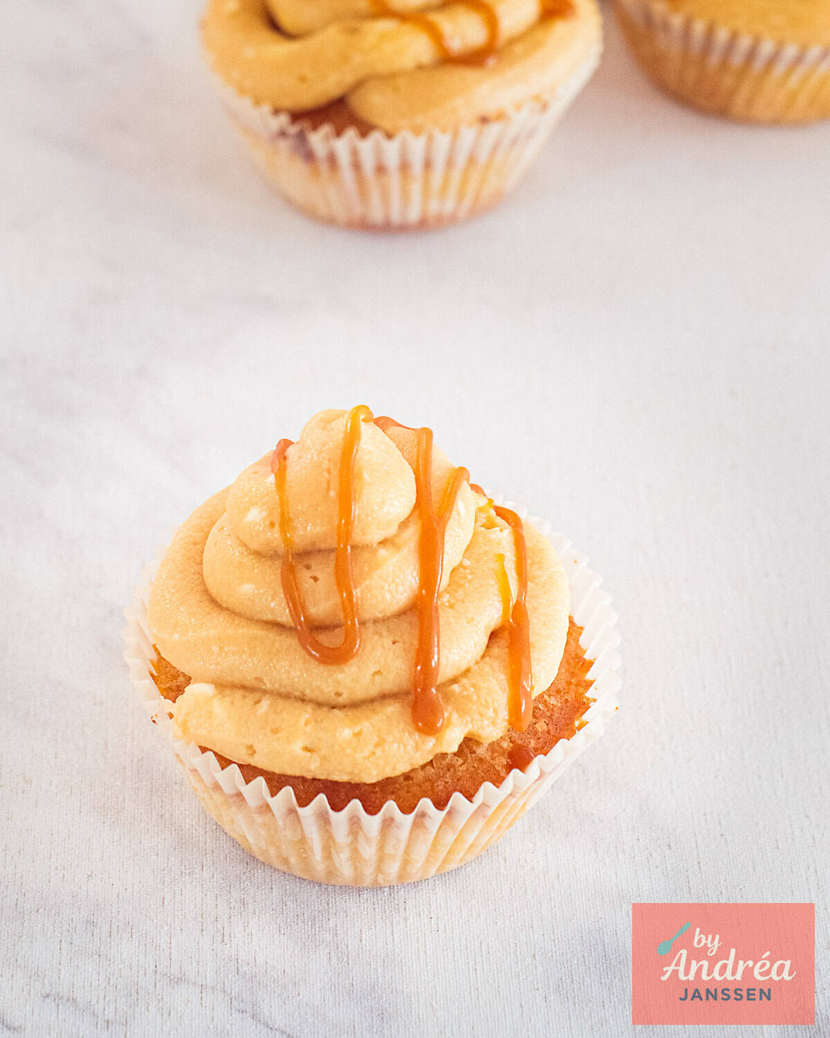 Een foto schuin van boven van een vanille cupcake met roomkaas frosting en salted karamel topping.