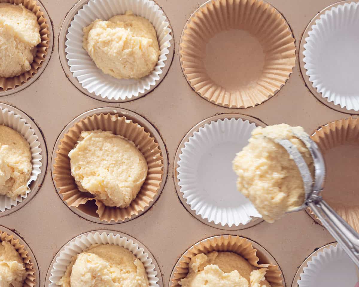 Een muffinblik met papieren bekers. Beslag wordt aan de bekers toegevoegd met een ijslepel
