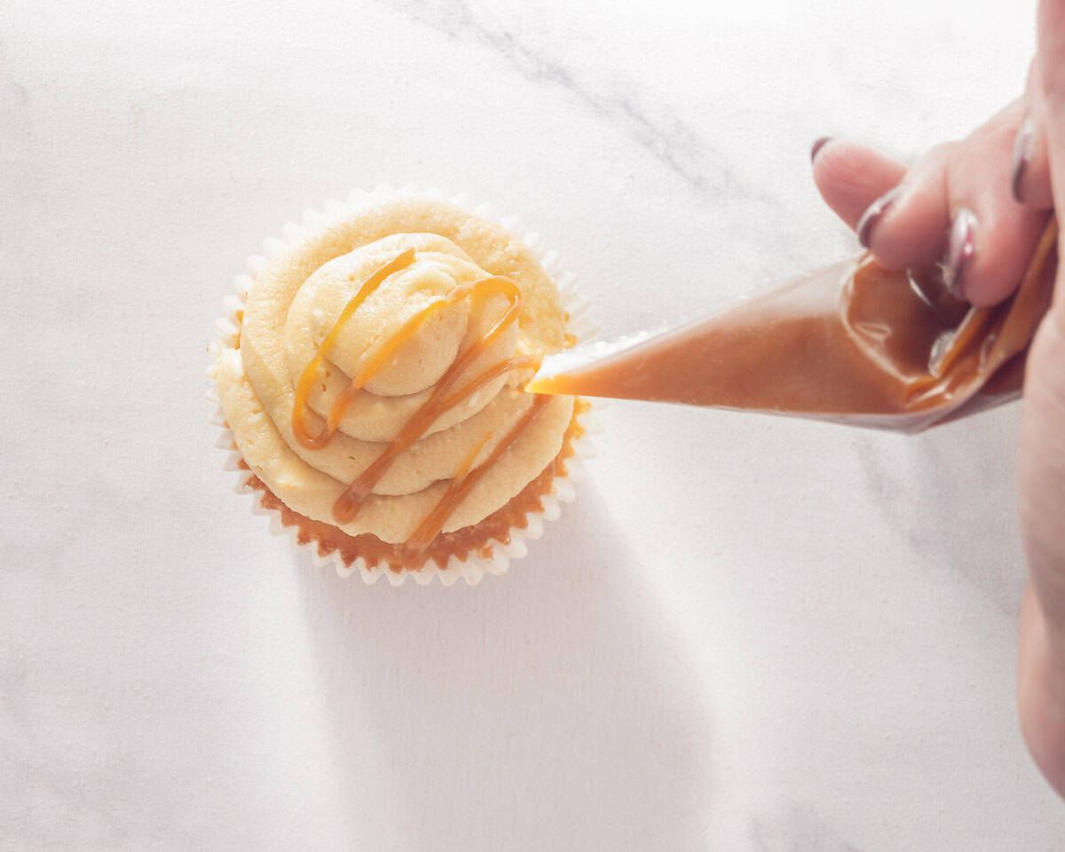 Een spuitzak spuit gezouten karamel op de bovenkant van de cupcakes