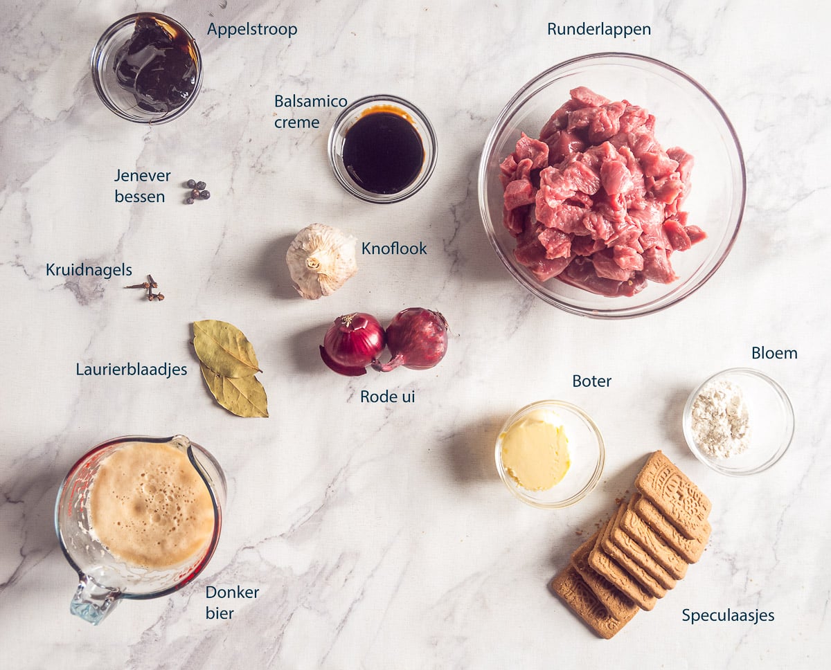 Ingrediënten voor de stoofschotel op een lichte ondergrond, met Nederlandse labels bij het rundvlees, de speculaas en overige ingrediënten.