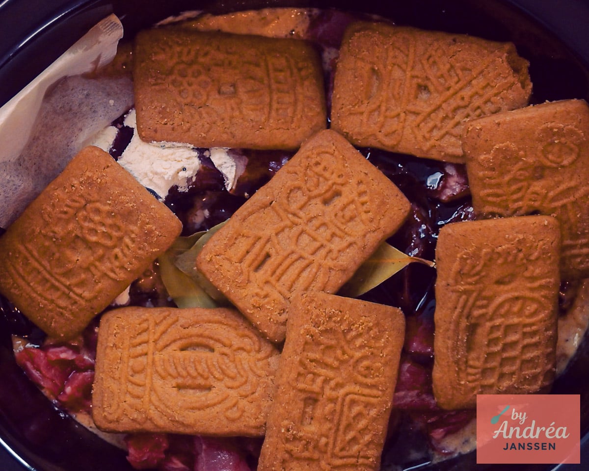 Hele speculaasjes liggen boven op het rauwe rundvlees en de overige ingrediënten in de slowcooker.