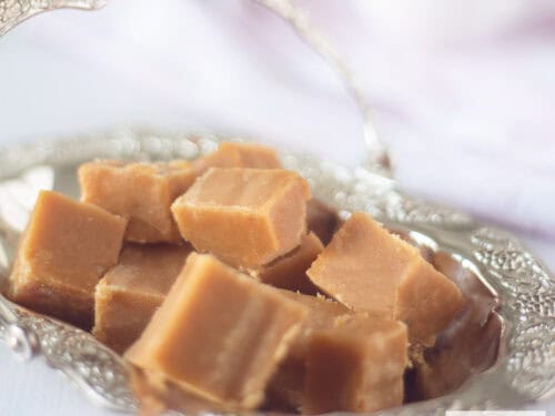 Een vierkante foto met een zilveren schaaltje met karamel fudge