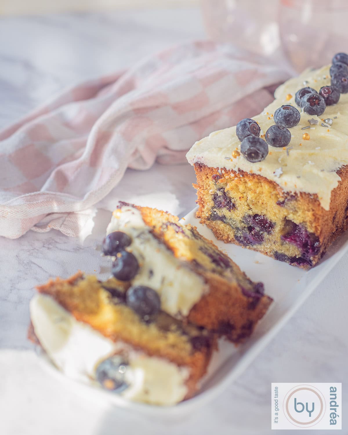 Een hoogtefoto van een blauwe bessencake met vanille frosting waar twee plakjes afgesneden zijn.