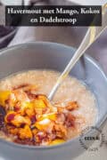 Een deel van een grijze kom met havermout met mango, kokos en dadelstroop. Een tekst bovenin: havermout met mango, kokos en dadelstroop