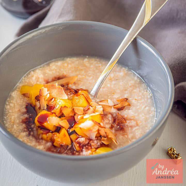 Een vierkante foto met een grijze kom met havermout, mango, dadelstroop en kokos