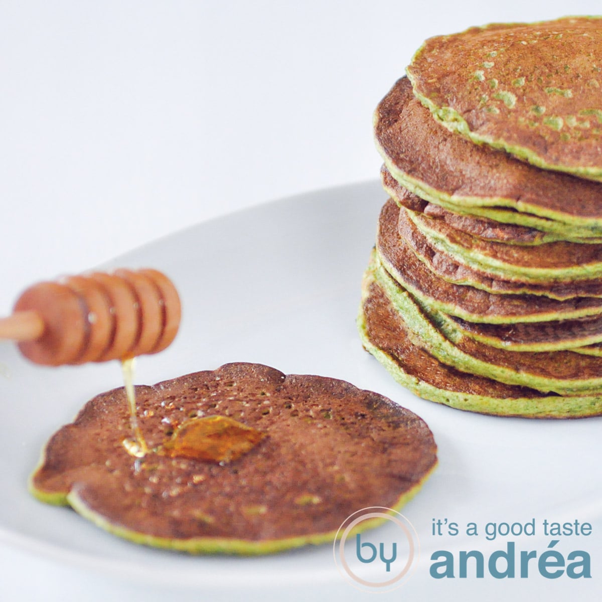 Vierkante foto, links een spinaziepannenkoek met een houten lepel met honing. Rechts een stapel spinaziepannenkoeken