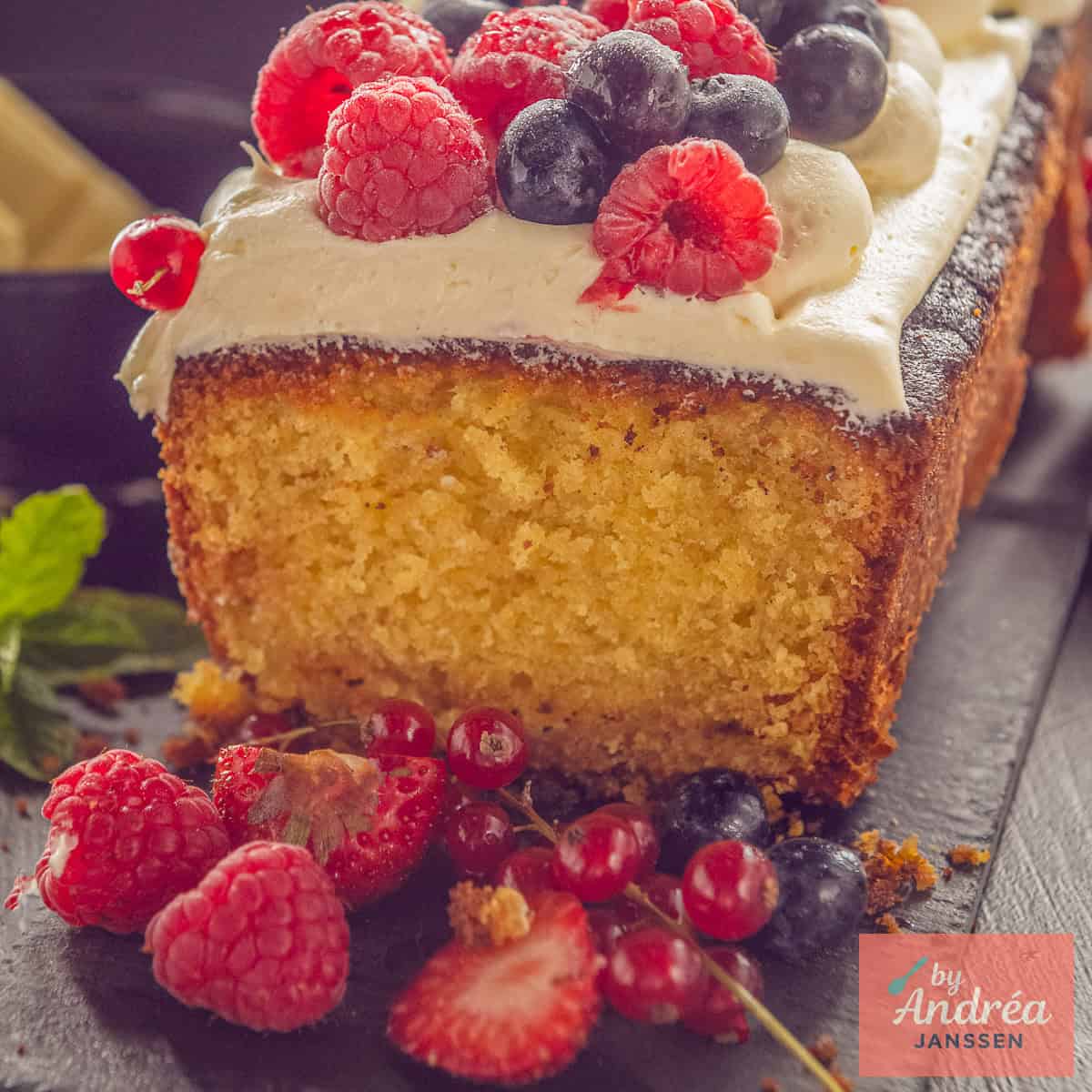 Een vierkante foto met een witte chocolade cake, botercrème en vers rood fruit op een donkere ondergrond.