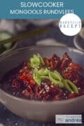 Deel van een grijze kom gevuld met langzaam gegaarde wortels en Mongools rundvlees, met een garnering van lente-ui. Een tekstoverlay eenvoudig recept, slowcooker Mongools rundvlees.