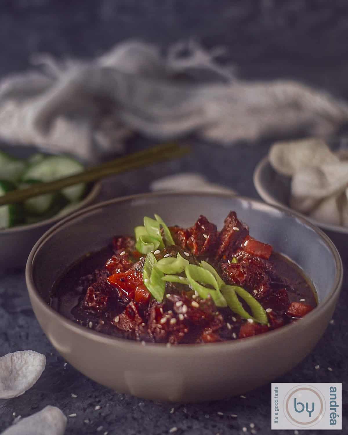 Een foto van een grijze kom gevuld met langzaam gegaard Mongools rundvlees, gegarneerd met lente uien.