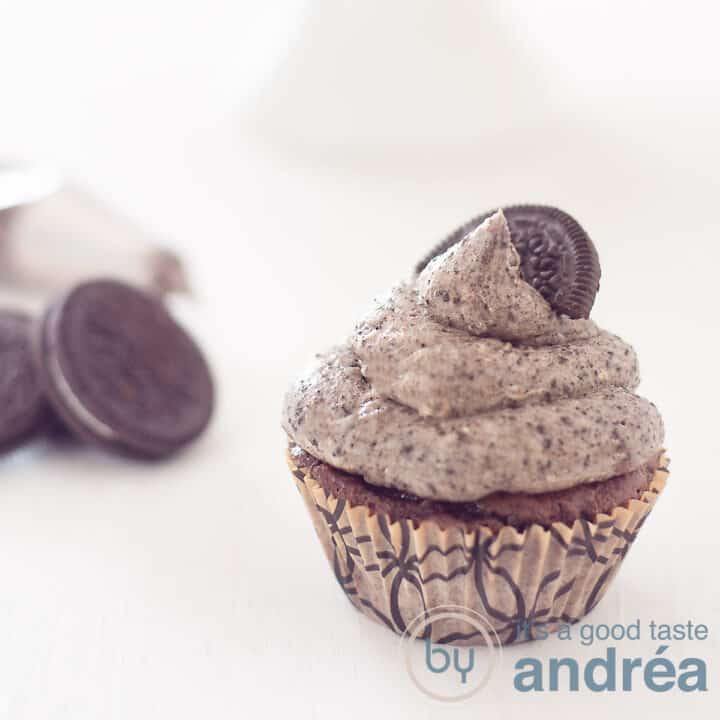 Een vierkante foto met een Oreo cupcake rechtsvoor. Links achter Oreo koekjes. Een witte ondergrond.