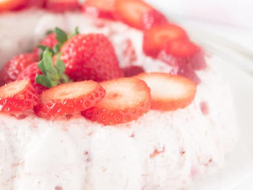 Een vierkante uitsnede van een bord met een halve aardbeienbavarois gedecoreerd met aardbeien.