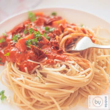Een vierkante foto met een bord spaghetti met saus met mascarpone, gehakt en tomaat.