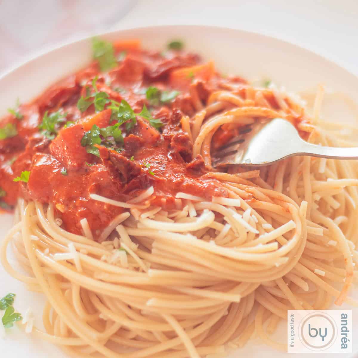 Een vierkante foto met een bord spaghetti met saus met mascarpone, gehakt en tomaat.