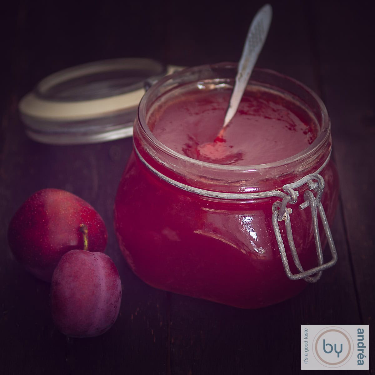 Een vierkante foto van een pot pruimenjam met 2 pruimen aan de zijkant.