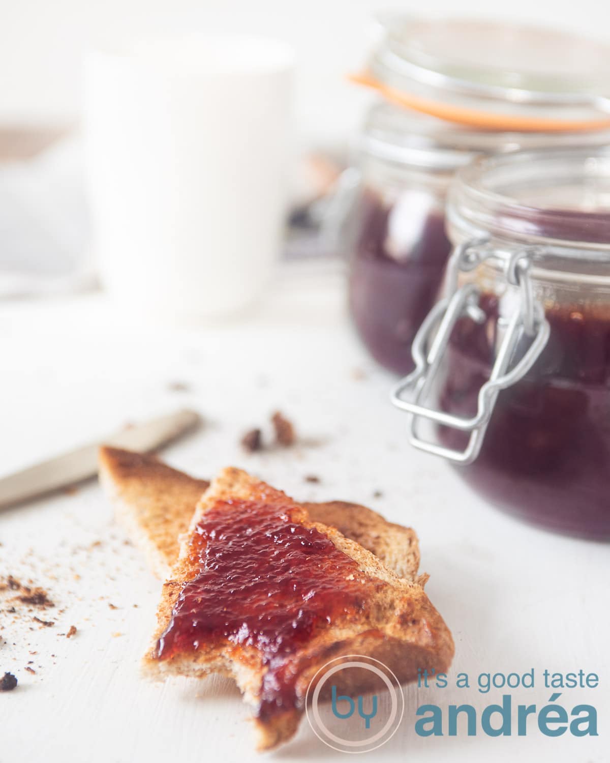 Twee geroosterde boterhammen besmeerd met pruimenjam. Twee potten op de achtergrond.