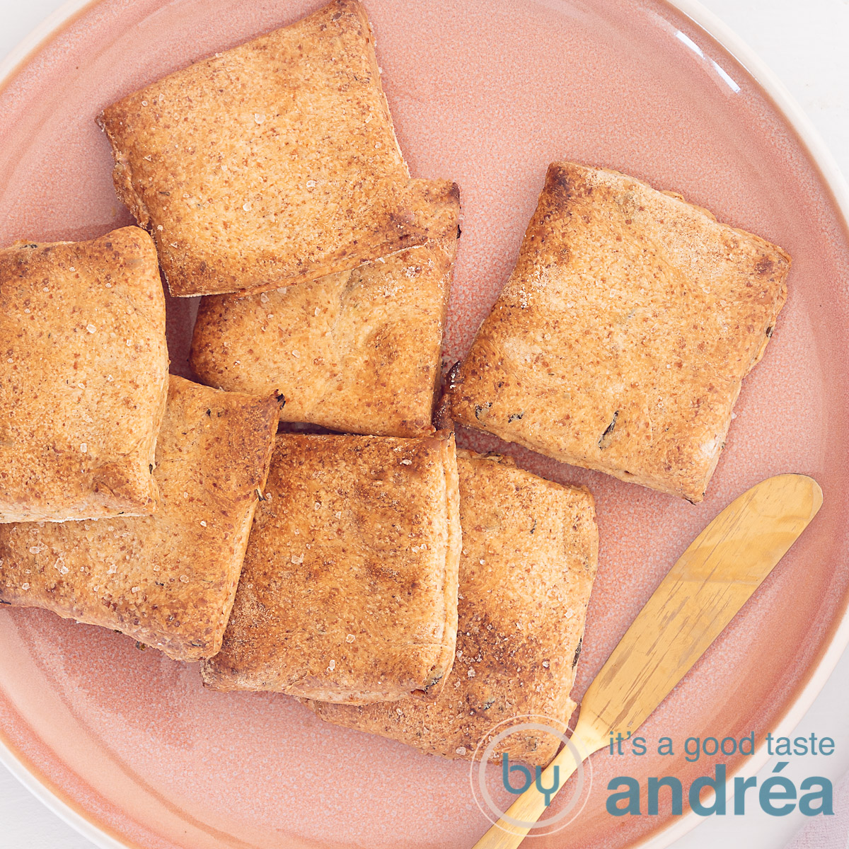 Een roze bord op een witte ondergrond gevuld met volkoren crackers met kruiden