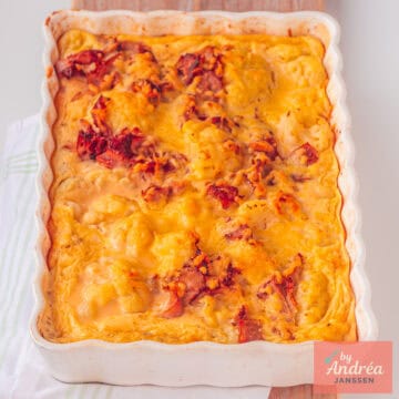 Een vierkante foto met een ovenschaal met gegratineerde bloemkool met spekjes.