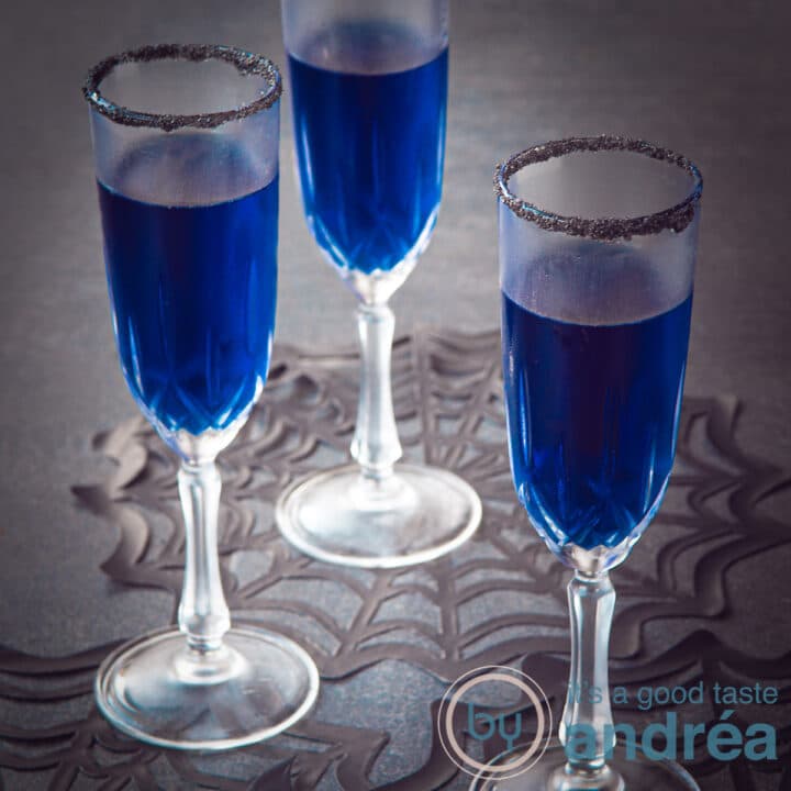 Een vierkante foto met een zwarte ondergrond, spinnenweb onderzetters en drie glazen gevuld met een blauwe cocktail