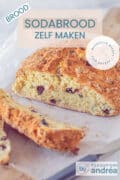 Een deel van een sodabrood met cranberry's en rozemarijn waar twee plakken af zijn gesneden. Een textoverlay bovenin: Brood, sodabrood zelf maken, makkelijk recept, zonder gist.