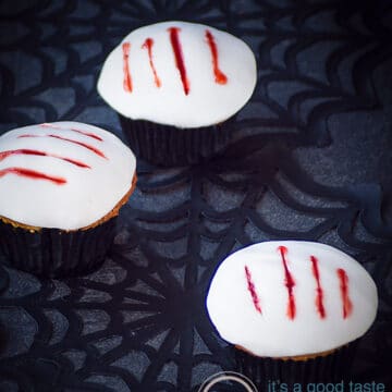 Drie cupcakes met een witte toplaag en vier klauw afdrukken gevuld met aardbeien bloed. Ze zijn geplaatst op een spinnenweb.