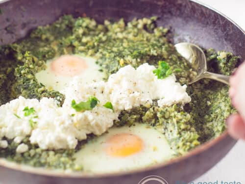 Een vierkante foto met een zwarte pan gevuld met een bloemkoolrijst, prei en spinazie schotel met ei en cottage cheese.