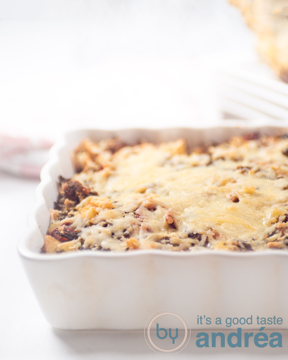 Een hoogtefoto met een halve witte ovenschaal gevuld met boerenkool en aardappels gegratineerd met kaas op een witte ondergrond