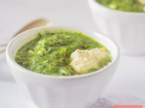 Een vierkante foto met twee kommen met rucola spinazie soep met creme fraiche.