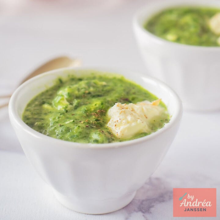 Een vierkante foto met twee kommen met rucola spinazie soep met creme fraiche.