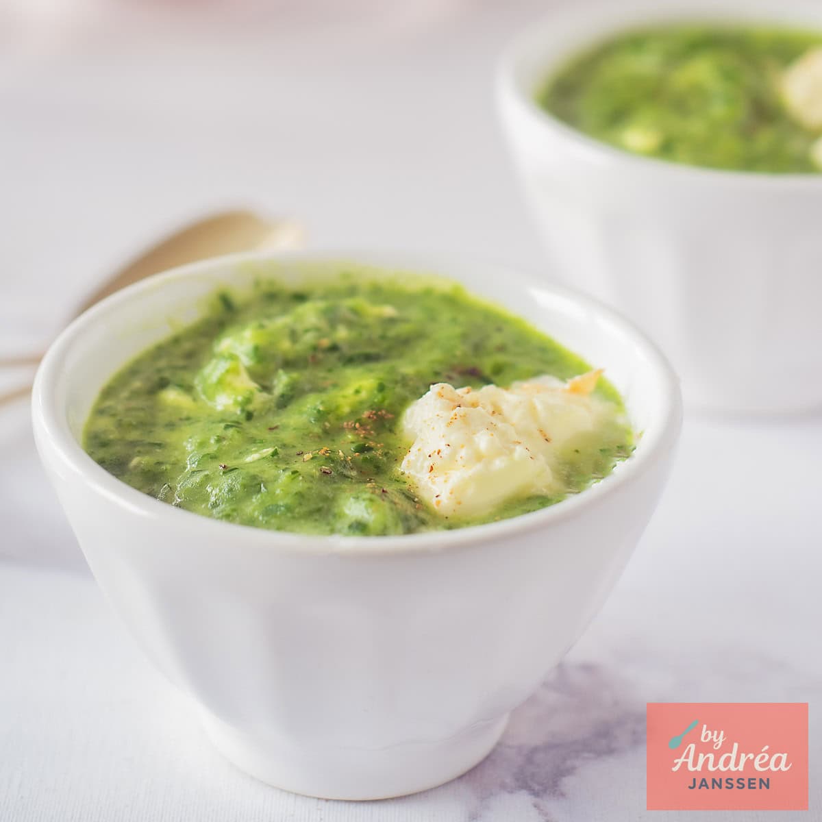 Een vierkante foto met twee kommen met rucola spinazie soep met creme fraiche.