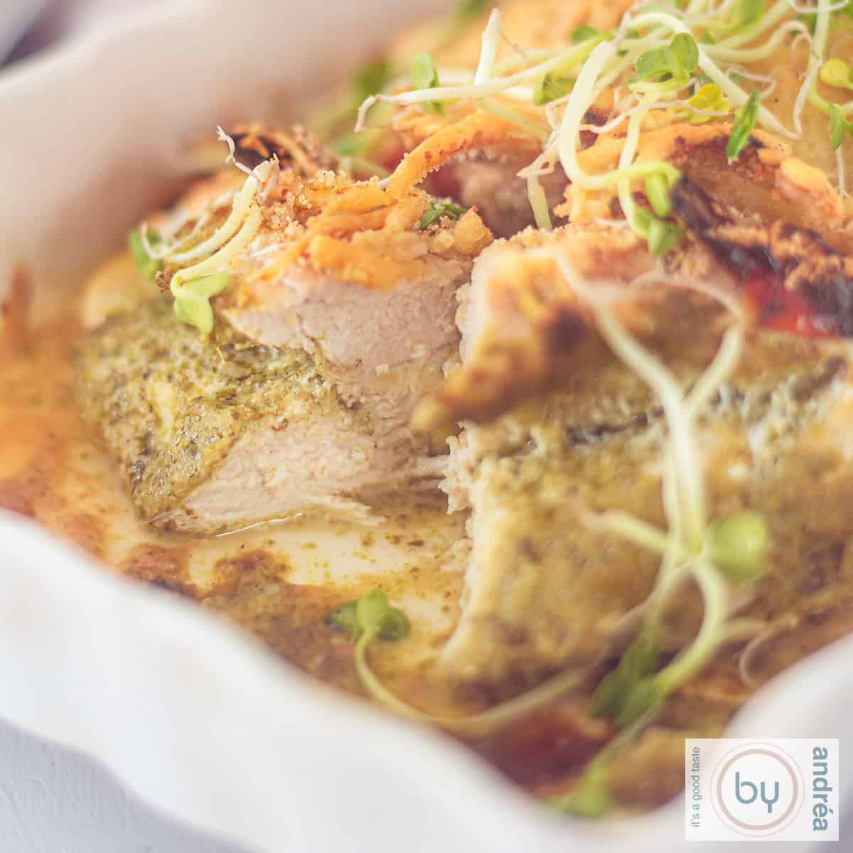 Een vierkante foto van een witte ovenschaal, deel, kipfilet met pesto en kaas