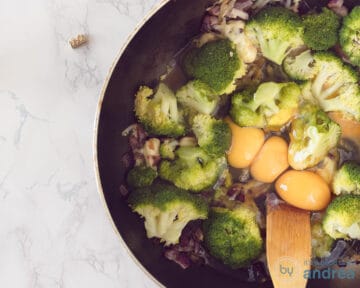 Een koekenpan met ui, kruiden en broccoli waaraan ei is toegevoegd.