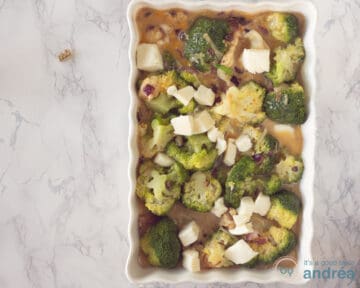 Een ovenschaal gevuld met broccoli, ei, ui, kruiden en Mozzarella op een marmeren ondergrond