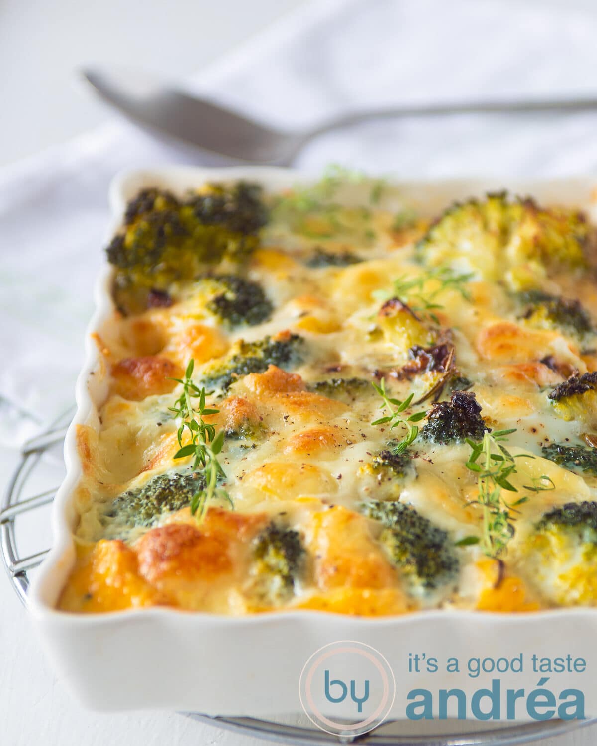 Een witte ovenschaal gevuld met eieren, broccoli en mozzarella gebakken in de oven. Een lepel op de achtergrond