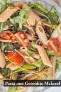 Een foto van bovenaf van een deel van pasta met makreel, tomaatjes en rucola met tapenade. Een tekst: pasta met gerookte makreel
