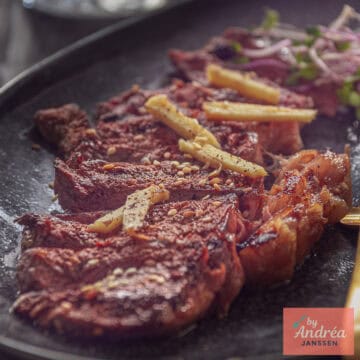 Een vierkante foto met een zwarte schaal met reepjes entrecote en sojasaus gember saus
