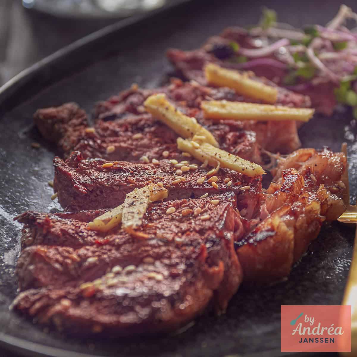 Een vierkante foto met een zwarte schaal met reepjes entrecote en sojasaus gember saus