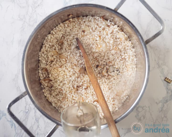 De aangebakken risotto wordt 'afgeblust' met wijn en bouillon