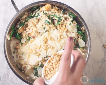 Aan de pan met risotto met kip en spinazie wordt Parmezaanse kaas en pijnboompitten toegevoegd