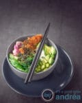 Een grijze kom gevuld met komkommer, sriracha, lima bonen, avocado en bieten. Getopt met zeewier.