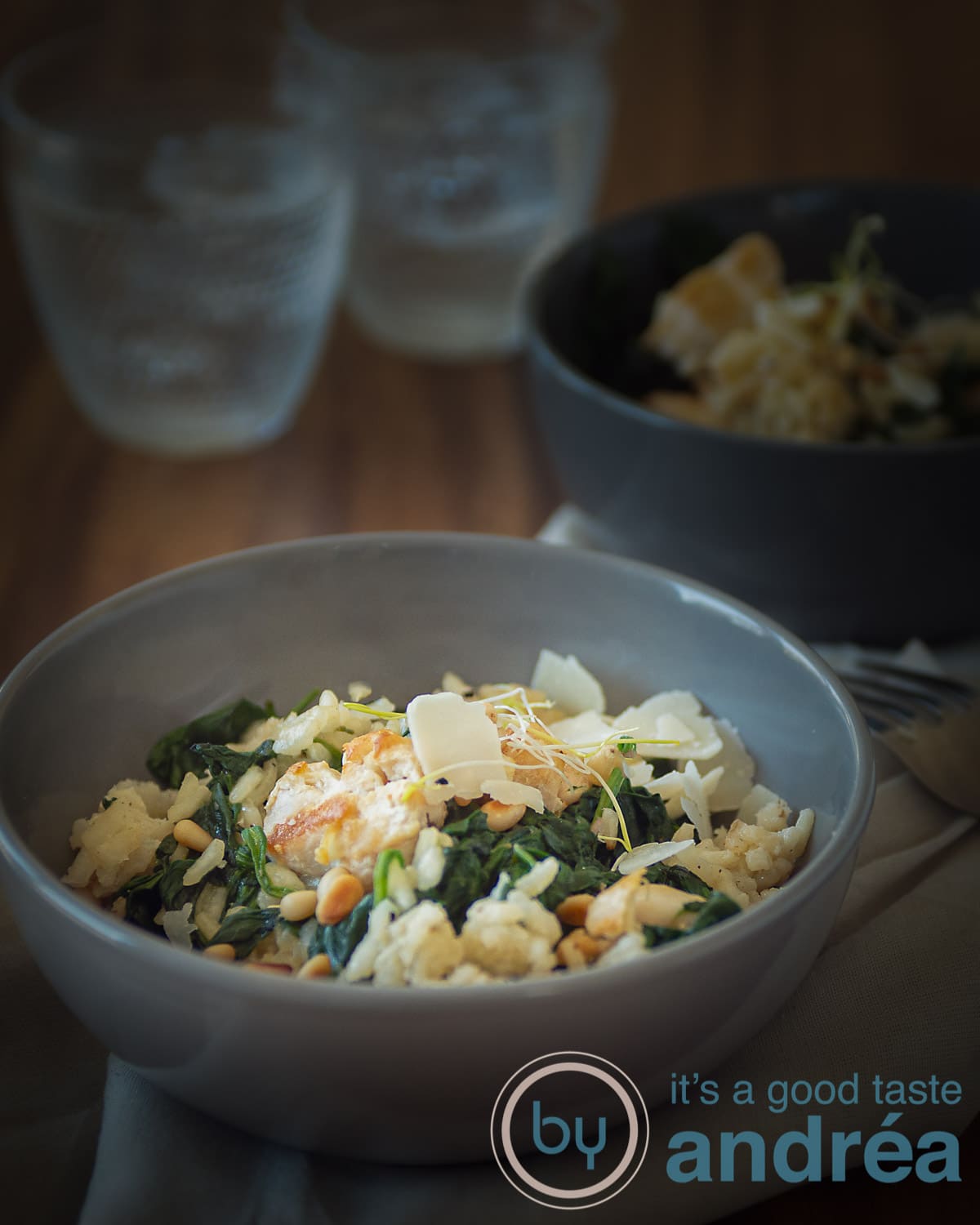a grey bowl filled with creamy risotto with spinach and chicken. Another bowl in the back as are two glasses
