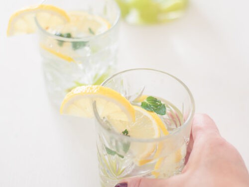 Een vierkante foto met twee glazen gevuld met fruitwater van druiven en citroen op een witte ondergrond.