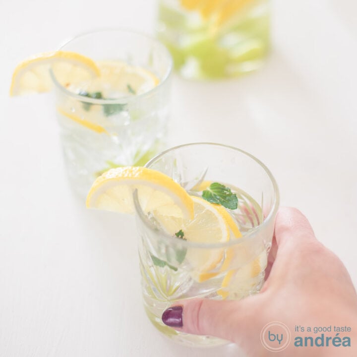 Een vierkante foto met twee glazen gevuld met fruitwater van druiven en citroen op een witte ondergrond.